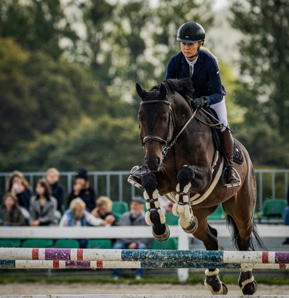 A woman and her horse gracefully jump a hurdle during a competitive equestrian event.